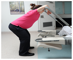 Pregnant woman squatting, resting her arms on a bar.