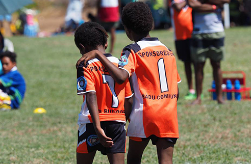 Children in jerseys walking the field, one child has their hand on the other child's back