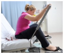 Pregnant woman sitting on a bed with legs wide apart, leaning forwards with arms on a bar in front of her.