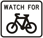 white sign with black words watch for, and an icon of a bicycle