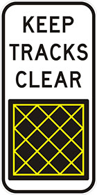 white sign with black text, keep tracks clear, and a black square panel with yellow cross hatching