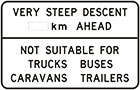 white sign with black text, very steep descent number of km ahead. Not suitable for trucks buses caravans trailers