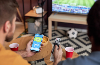 2 young males watching sport and looking at their phone.