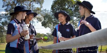 Group of children talking over tennis net.