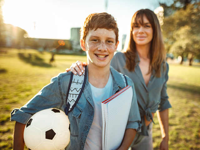 a fair skinned child with a ball and book, a fair skinned female with her hand on the boys shoulder