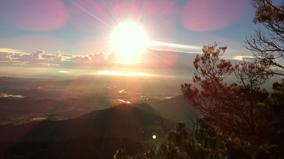 Sunrise at Lamington National Park in the Gold Coast hinterland, with the brilliance of the sun offset by trees and rolling valleys in the distance.