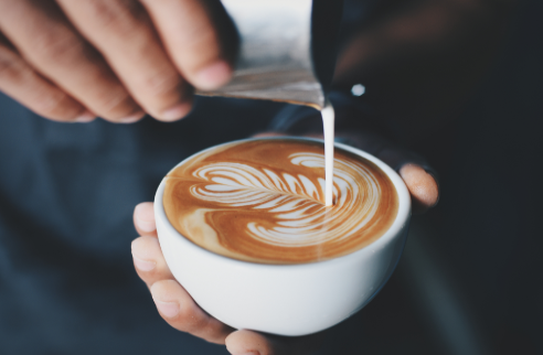 barista pouring milk into coffee