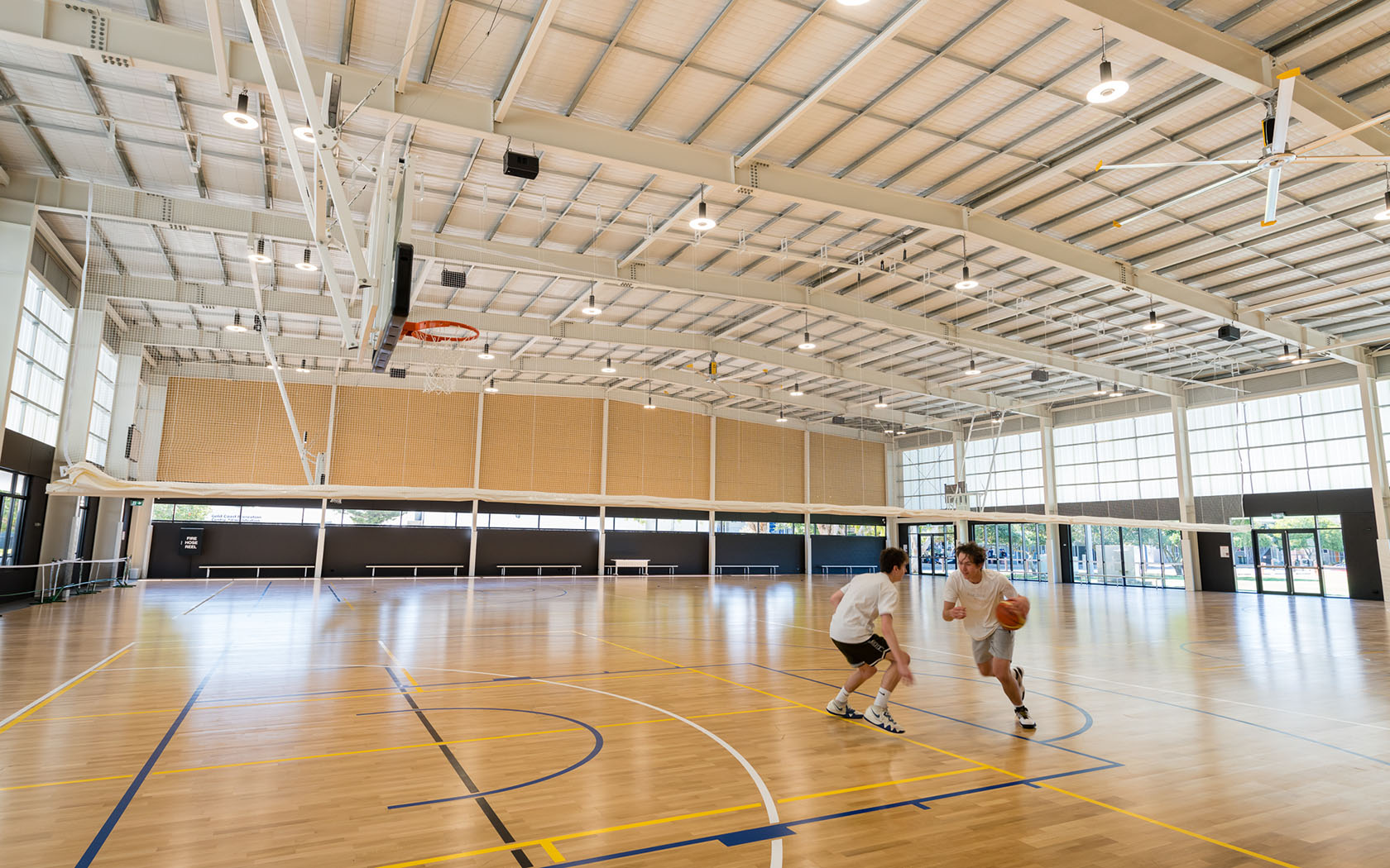 Two men playing basketball in an indoor court, one dribbling the ball and dodging the the other player. 