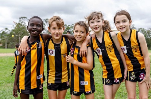 Group of young AFL players huddled together on a green field. 