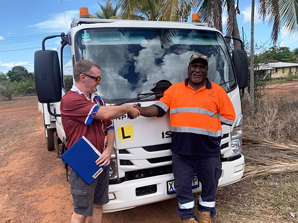 Two people shaking hands in front of truck displaying learner L plate