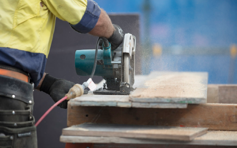 photo of back of a construction worker using power saw on wood