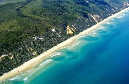 Aerial view of a blue ocean, a sandy beach and coloured sand cliffs