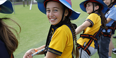 Children wearing sun safe clothing and safety harness playing tug of war outside. 