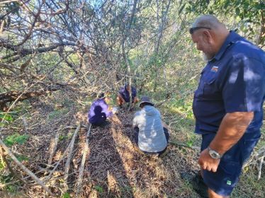 Rangers setting up a camera in a bush clearing.