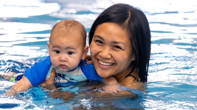 A mother in a pool holding a baby up above the water