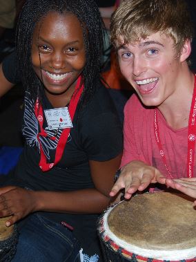 A young woman and man smiling, playing bongos.