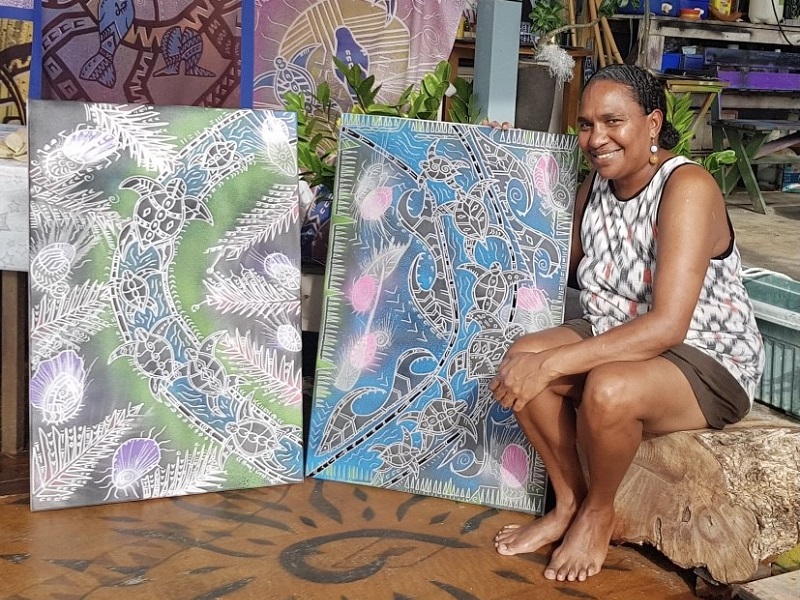 Moana sits barefooted with a selection of her artworks
