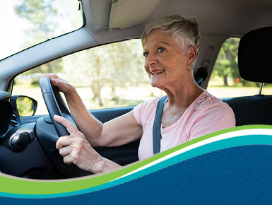 An older woman in car holding the steering wheel and looking out the window smiling.