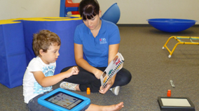 A speech pathologist from the AEIOU Foundation uses an iPad with a young boy who participates in an early intervention program.