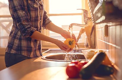 Woman washing capsicum in kitchen sink