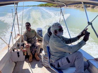 Three rangers in a small boat on a river videoing mangroves.