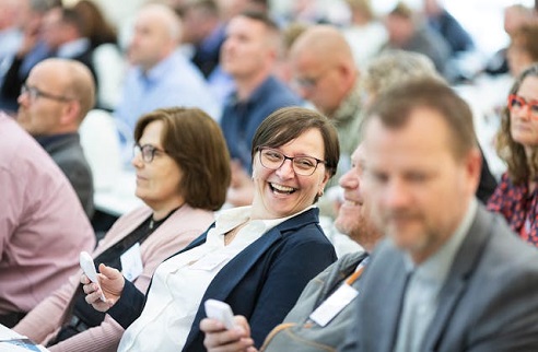 A group of people sitting in a room with one person in focus and the rest blurred