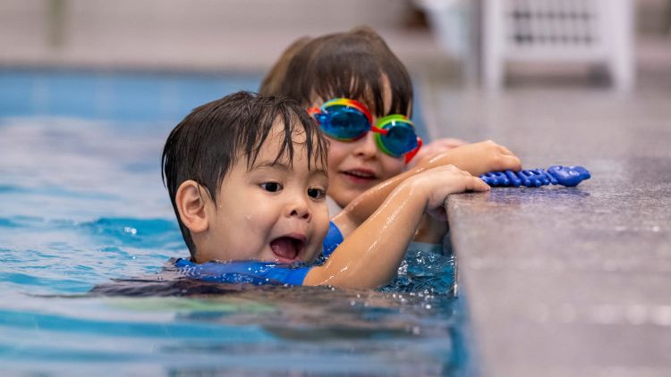 Young swimmers holding onto the side of the pool