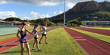 Three people in sports gear at the Townsville Sports Precinct holding pole vaults and looking at the camera.