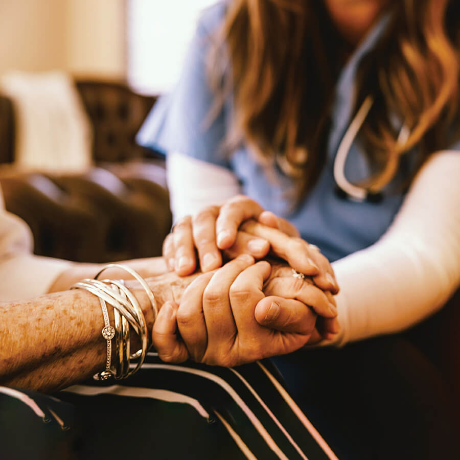 A young woman holds the hands of an older woman.