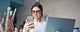 young girl smiling while looking at a mobile held in one hand, sat amongst work/hobby items