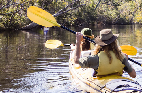 Two people paddling in a kayak in a creek with trees in the background